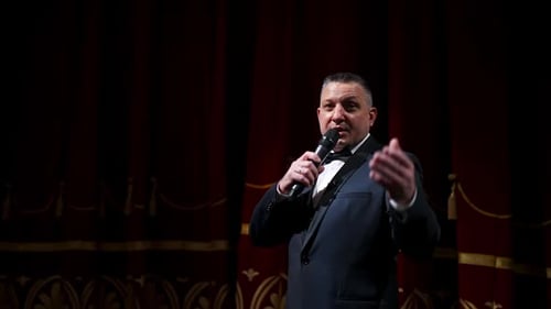 Actor with microphone announces performance before auditorium. Theater curtains background.