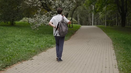 Caucasian Man Puts Backpack on Back While Walking in Park