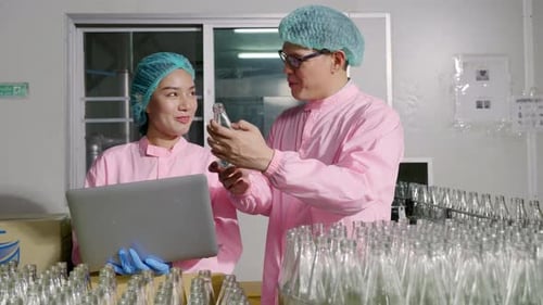 Deux ingénieurs supervisent le contrôle qualité en vérifiant les bouteilles de produits sur le tapis roulant d'une usine de boissons