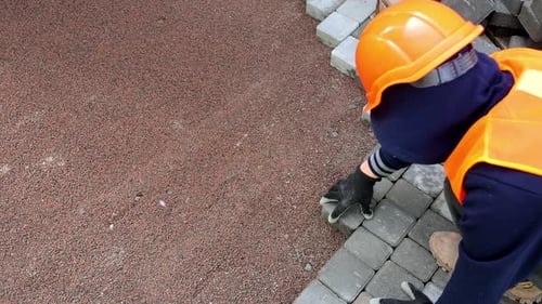 Worker Installing Pavement Blocks A Worker in Orange Safety Gear Carefully Places Interlocking