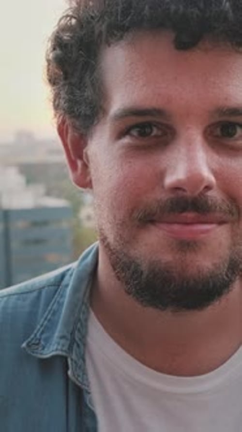 Close-up of smiling young guy posing at the camera while standing on the balcony