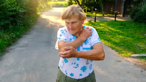 Elderly Woman Rubbing Sore Elbow Outdoors