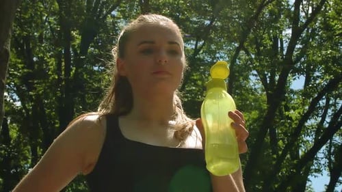 Athletic Woman Holding Water Bottle in Sunny Park