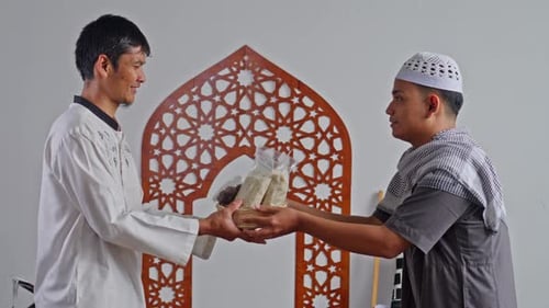 Muslim man giving rice Zakat Al-Fitr to another man and shaking hands during Ramadan in mosque