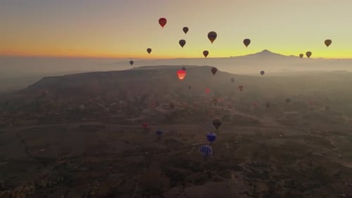 Drone view of hundreds of colorful hot air balloons soaring at sunrise in Cappadocia