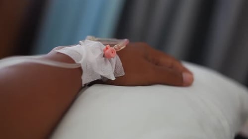 Close up IV drip solution in a patient's hand while lying on bed in hospital.