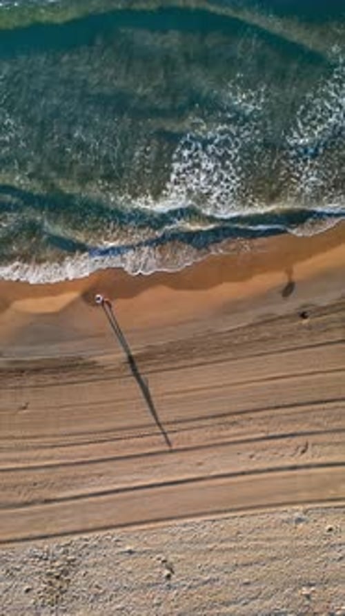 Man walking on the beach with waves hitting the shore in Alicante, Spain. Vertical