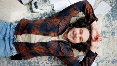 Portrait of a Happy Brunette Guy with Curly Hair in a Checkered Shirt Who Falls on a Pillow on the