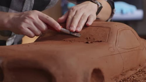 Close Up Of Man Automotive Designer's Hands Using Rake Or Wire To Create Details In Car Clay
