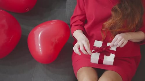 Woman Untying a Gift Near Red Heart Balloons