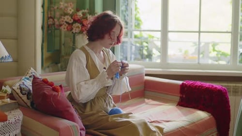 Woman Knitting with Blue Yarn on Sofa Indoors
