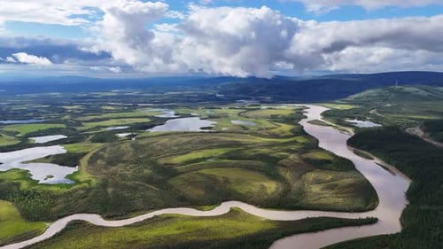 Dramatic aerial view of meandering river flowing through lush green landscape under dynamic cloudy