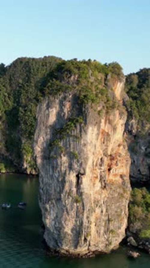 Aerial drone view of a limestone sea stack rising from calm tropical waters in southern Thailand. Ve