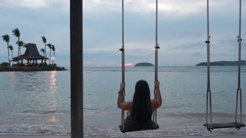 Rear View of Young Woman Having Fun Swinging on Beach Swing By The Sea At Sunset, Shangrila Resort,