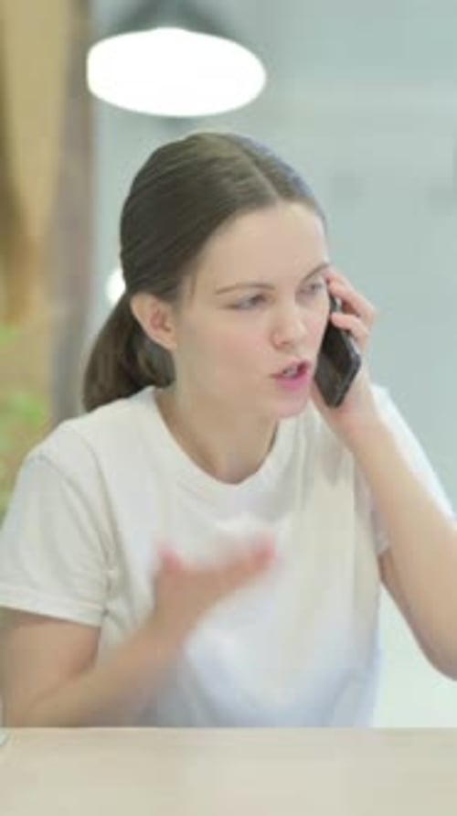 Frustrated Woman Talking on Phone at Table