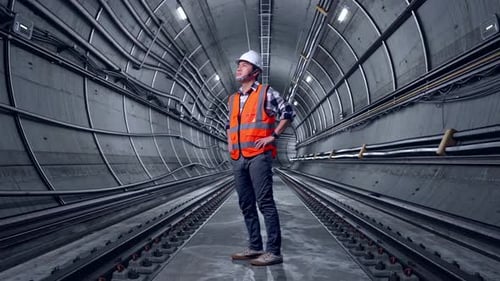 Full Body Side View Of Asian Male Engineer Looking Around With Arms Akimbo In Subway Tunnel