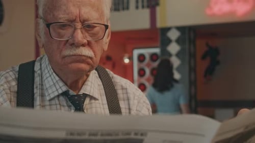 Serious Gentleman in Glasses Paging Through Morning Newspaper in Diner