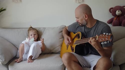 Father Plays Guitar for Daughter on Couch