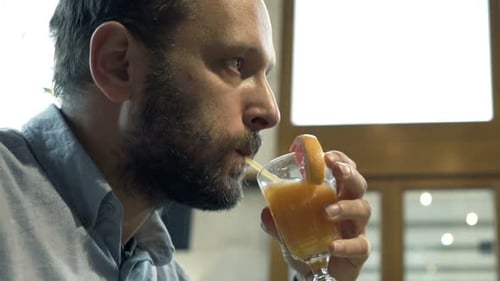 Young, Happy Man Relaxing and Drinking Orange Juice in Cafe 30s