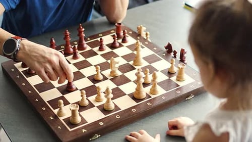 Vater bringt seiner kleinen Tochter das Schachspielen am Tisch in der heimischen Küche bei
