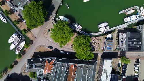 An overhead drone view of a charming canal with boats docked along the edges, a bridge crossing