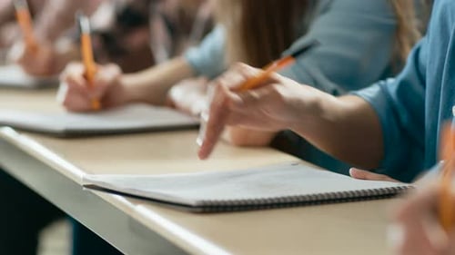 Close-up of the Row of Students Writing in the Notebooks, Taking Exam. Focus of Hands with Pens.