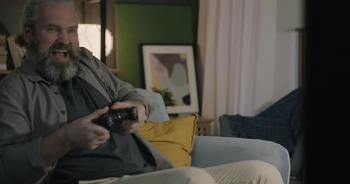 Bearded Man Playing Video Games at Home on Sofa