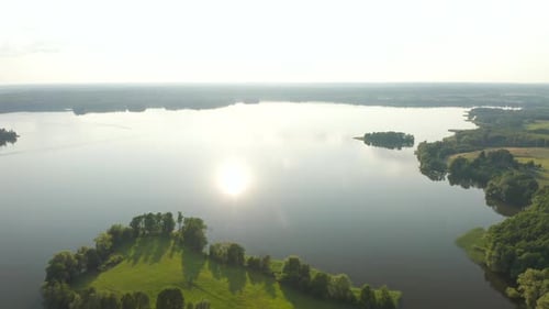 Aerial view of a scenic lake with sun reflection and surrounded by green farmland.