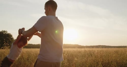 Happy Father Spinning His Son Holding Hands in a Golden Field at Sunset