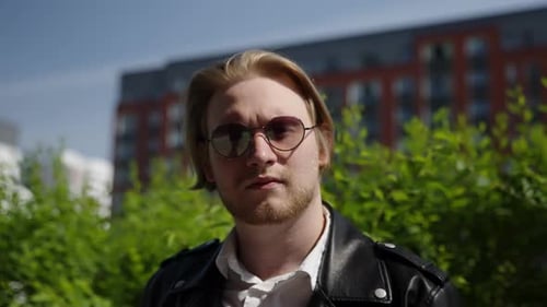 Fair-haired man poses in black jacket and sunglasses