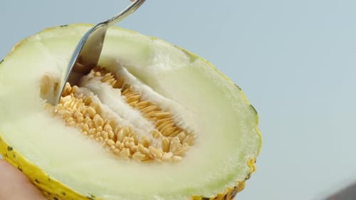 La moitié d'un melon jaune avec des os, cueillant les os avec une cuillère, sur fond de ciel bleu, gros plan