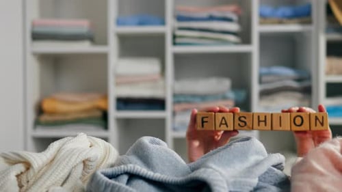 Hands Hold Fashion Blocks Over Pile of Clothes