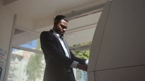 Seitenansicht eines verwirrten afrikanischen Geschäftsmannes, der Probleme mit einem Geldautomaten hat. Junger Mann stößt auf einen