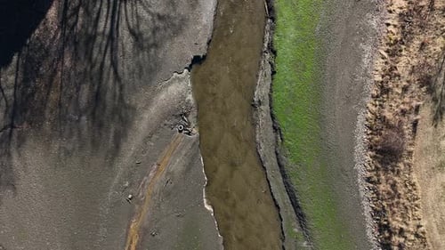 A dry riverbed with sparse green grass and eroded terrain on a sunny day , aerial view
