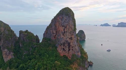 Boats cruise near limestone cliffs at Railay Beach during sunset