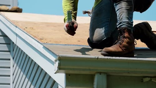 Worker Using Nail Gun on Suburban House Roof