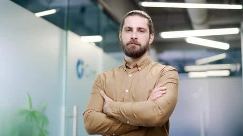 Portrait of serious bearded businessman standing with crossed arms at workplace in a business office