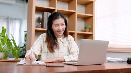 Beautiful Asian office worker, sitting working on laptop computer placed on table in front, with