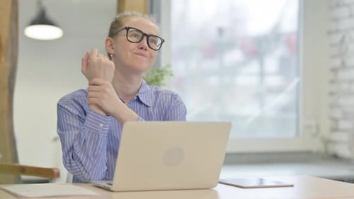 Woman Massaging Sore Wrist While Using Laptop