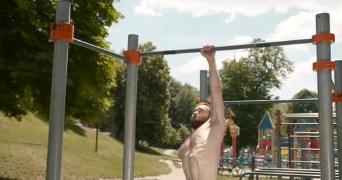 Young Man Doing Pull Ups on a Bar in the Park