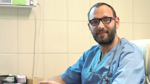 Happy male doctor portrait sitting at his desk in a bright hospital office