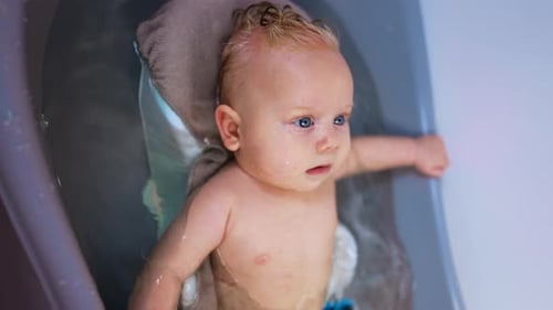 Relaxed Caucasian infant lies in the water. Lovely cute baby boy having a bath. Close up.