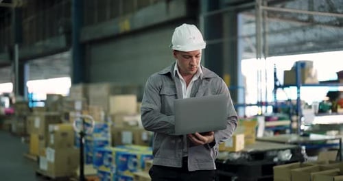 caucasian male warehouse operator using laptop to check inventory tracking system while standing