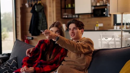 Young couple in love together sitting on the sofa at home watching comedy film and laughing