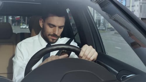 Man Sits in Car Looking at his Mobile Phone