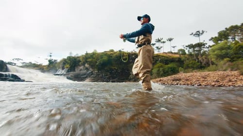 Man Wades in River Fly Fishing Near Waterfall