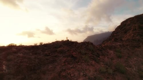 Woman stands on a rocky peak, watching the sunset over the ocean in Tenerife, Canary Islands, Spain.