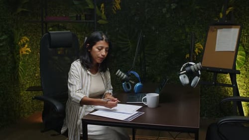Female Podcast Host Taking Notes on Paper at Work in Recording Studio