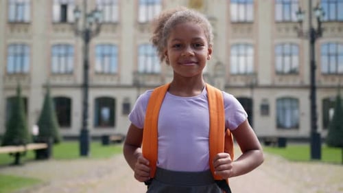 Smiling Girl with Backpack in Front of School