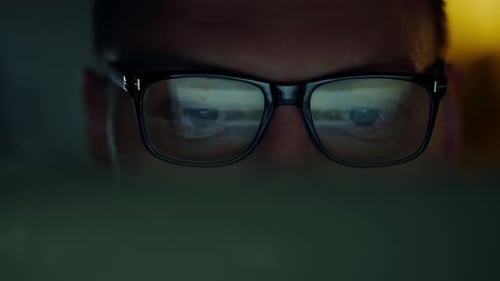 IT programmer, a man with glasses, works at night with a portable laptop. His face expresses